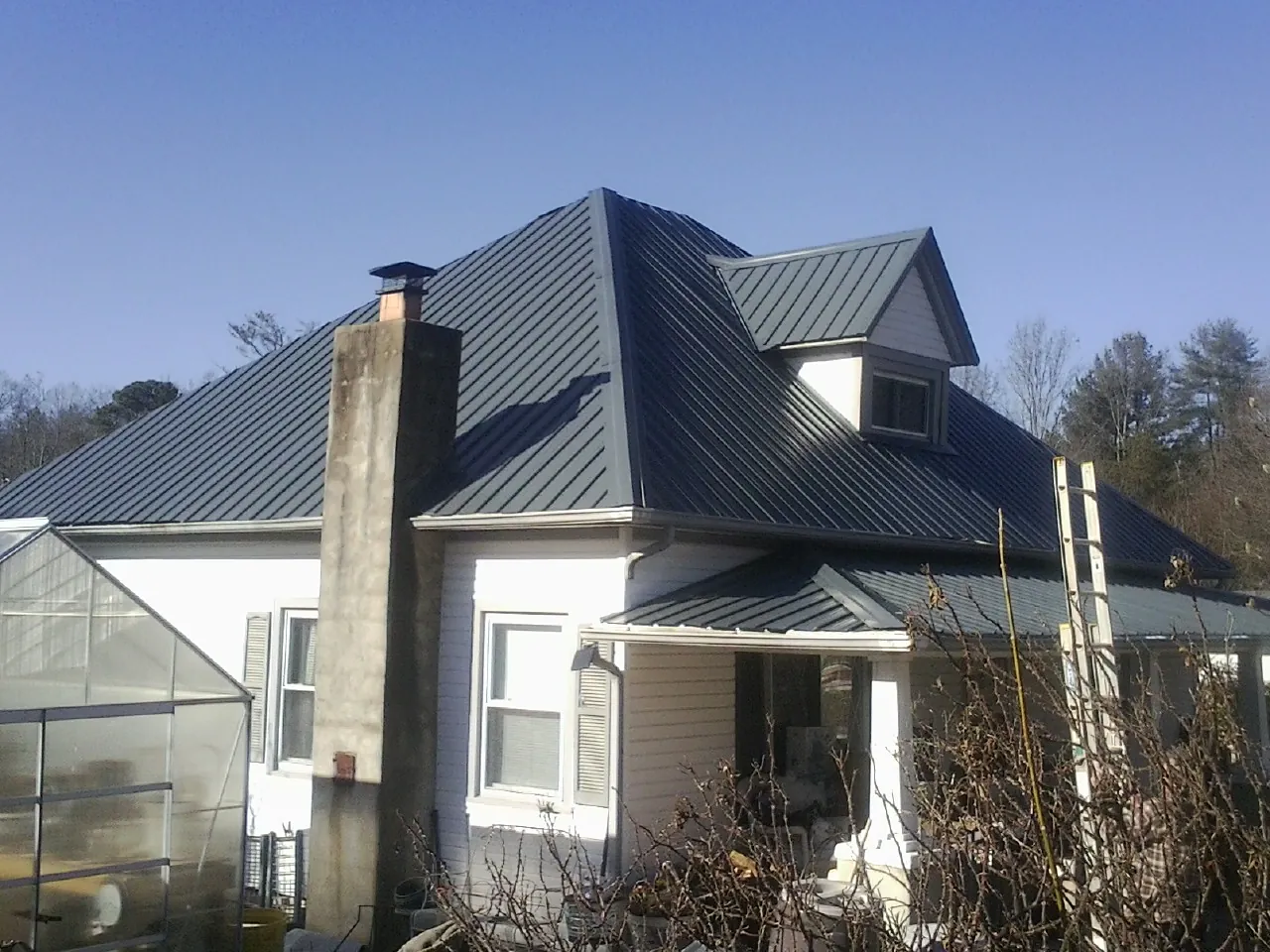 Dark blue standing seam metal roof on a white farmhouse with dormer — Slate & Tile Roof Repair by Roofing Brothers in Townsend