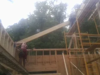 Carpenter raising a rafter beam on a new second story frame in Townsend