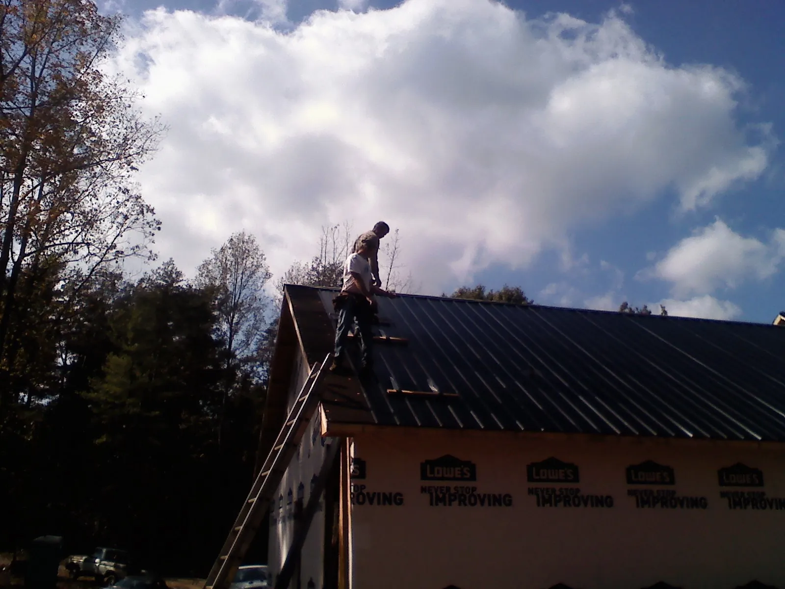 Roofer fastening dark metal panels high against a cloudy sky, from a Roof Inspection job in Townsend